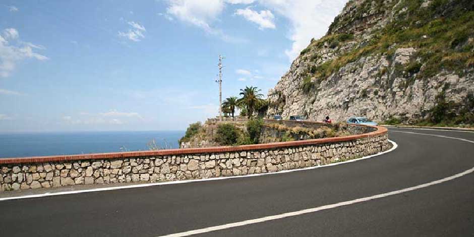 Route côtière sinueuse bordée d'un muret en pierre longeant une falaise avec vue sur la mer.