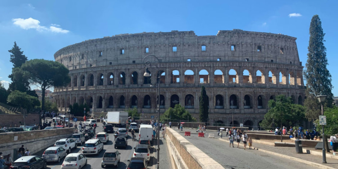 Vue imposante du Colisée de Rome dominant une avenue animée par le trafic urbain sous un soleil radieux.