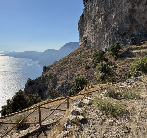 Sentier escarpé bordé d'une barrière en bois surplombant la mer sur le Sentier des Dieux.
