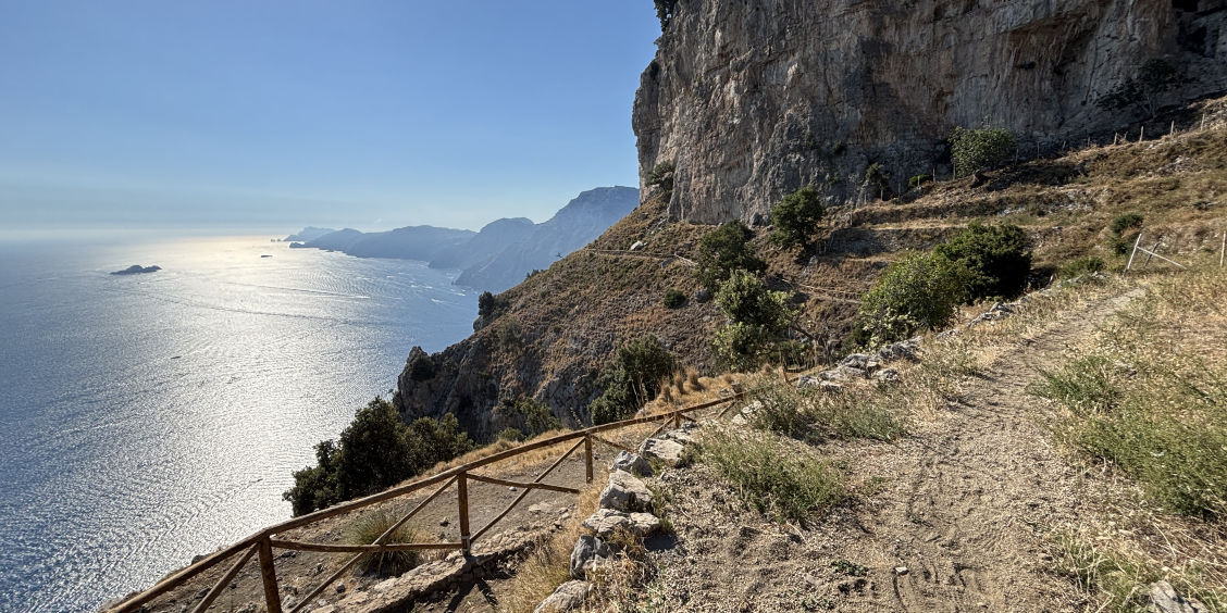 Sentier escarpé bordé d'une barrière en bois surplombant la mer sur le Sentier des Dieux.