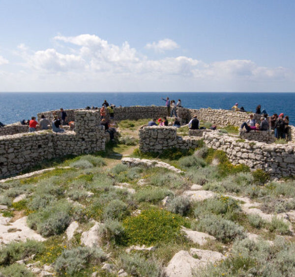 Ruines d'un fortin en pierre sur le sentier des Fortins à Capri avec des randonneurs et vue sur la mer.