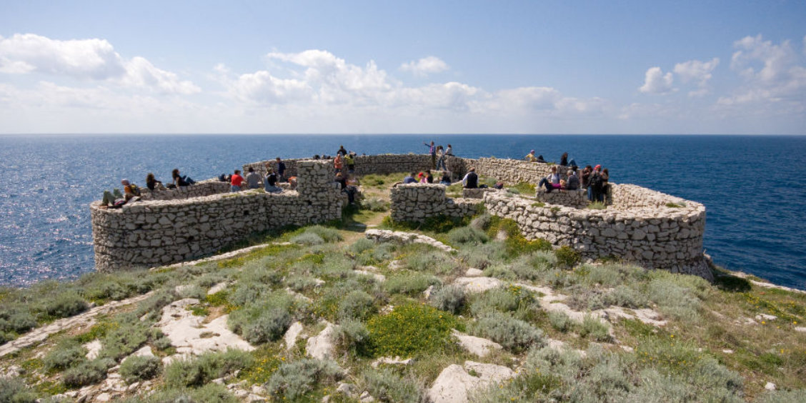 Ruines d'un fortin en pierre sur le sentier des Fortins à Capri avec des randonneurs et vue sur la mer.