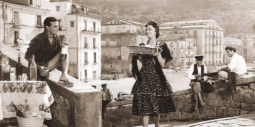 Scène de film en noir et blanc tournée à Marina Grande à Sorrente avec acteurs et village en arrière-plan.