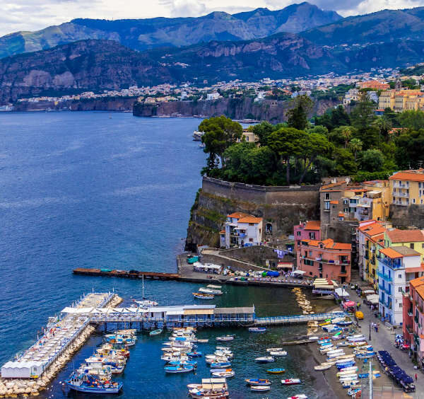 Vue panoramique de la côte de Sorrente, en Italie : falaises de tuf calcaires spectaculaires, bâtiments colorés accrochés au relief et un port pittoresque rempli de bateaux.