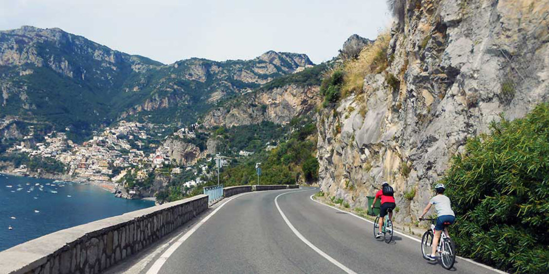 Balade à vélo sur la Côte Amalfitaine avec cyclistes, falaises et vue sur Positano.