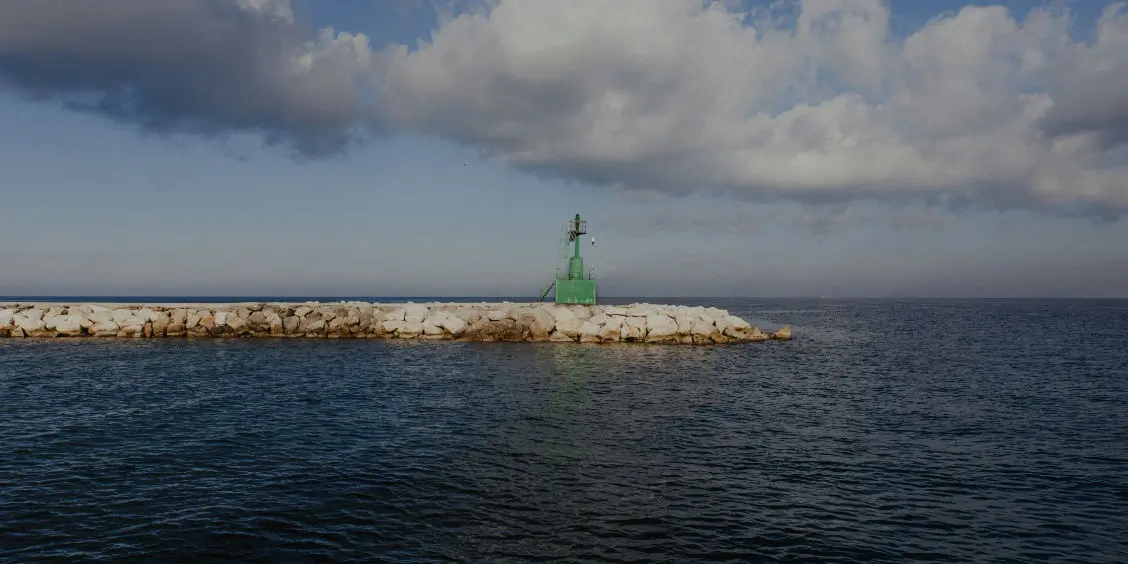 Une jetée en pierre surmontée d'un phare vert au milieu des eaux.