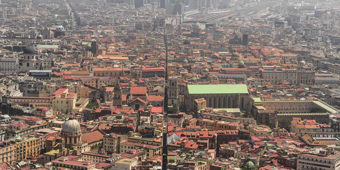 Vue aérienne de Naples montrant la célèbre rue Spaccanapoli fendant le centre historique et ses toits de tuiles rouges.
