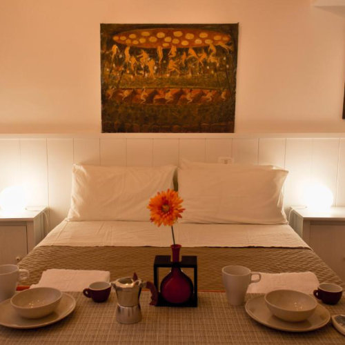 Chambre accueillante avec un lit double surplombé d'un grand tableau d'art, et une table dressée pour le petit-déjeuner avec une moka italienne.