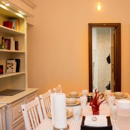Intérieur lumineux d'un appartement napolitain montrant un coin repas avec une table blanche dressée et une bibliothèque murale.