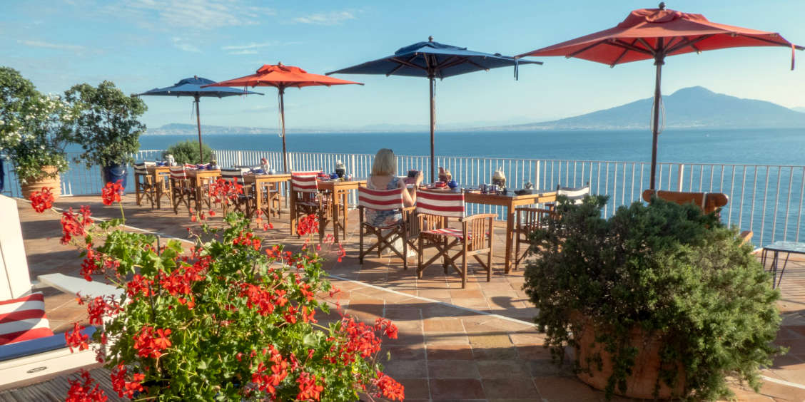 Une terrasse ensoleillée en bord de mer offrant una vue panoramique sur le golfe de Naples et le Vésuve.