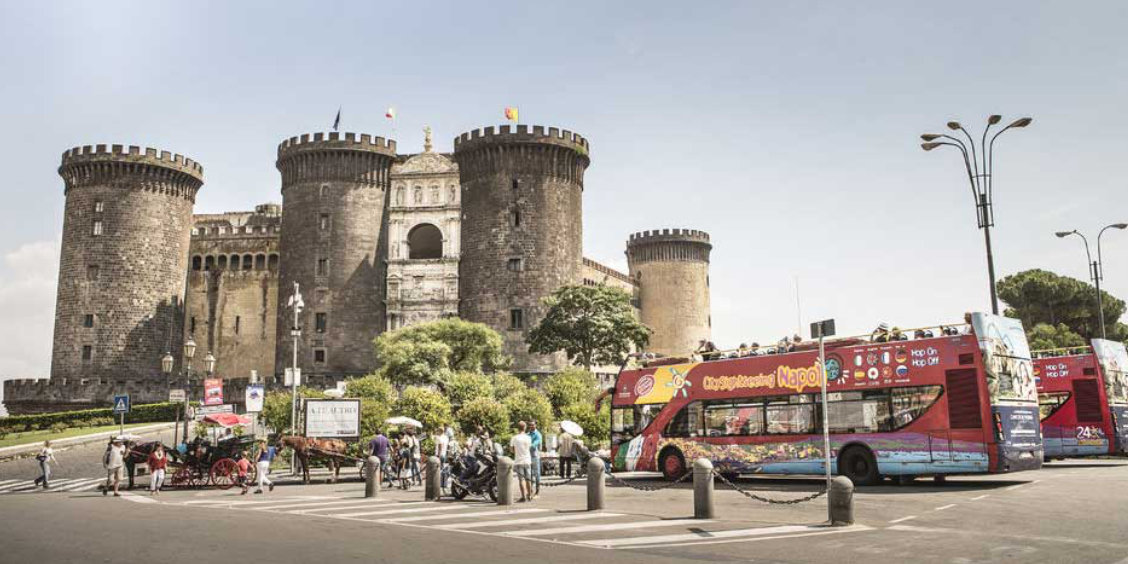 Bus touristique à Naples près du Castel Nuovo, avec visiteurs et circulation en centre-ville.