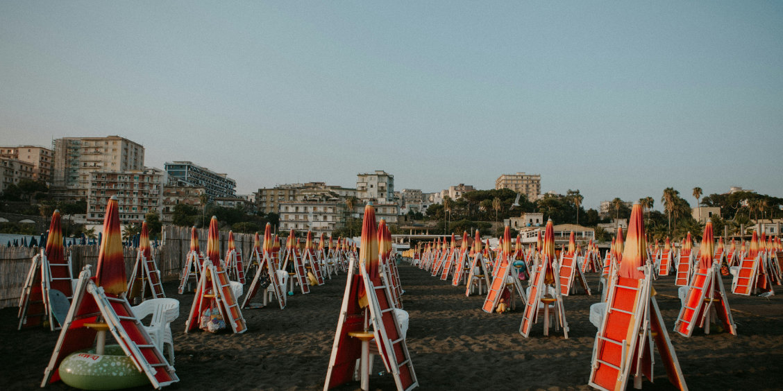 Plage de sable noir à Torre Annunziata avec de nombreux parasols et transats orangés pliés, devant les immeubles de la ville.