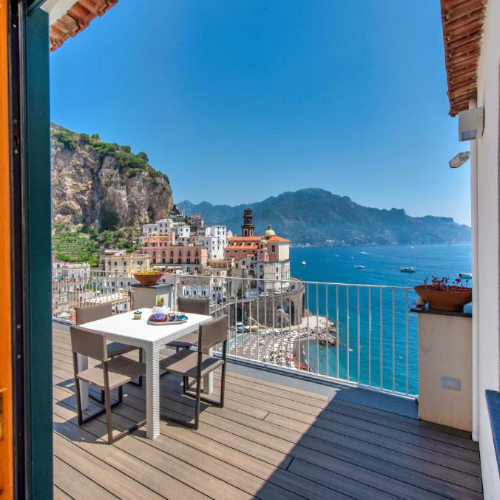 Terrasse panoramique avec table et chaises offrant une vue sur le village d'Atrani et la mer.