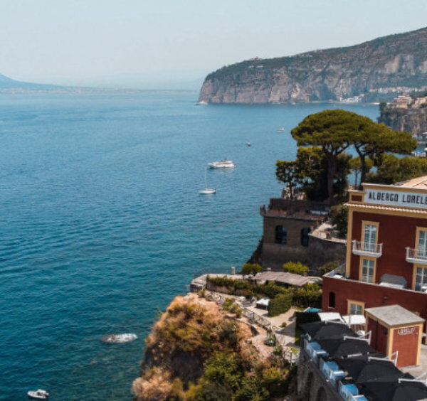 Vue panoramique de Sorrente avec hôtels sur les falaises, mer bleue et Vésuve au loin.
