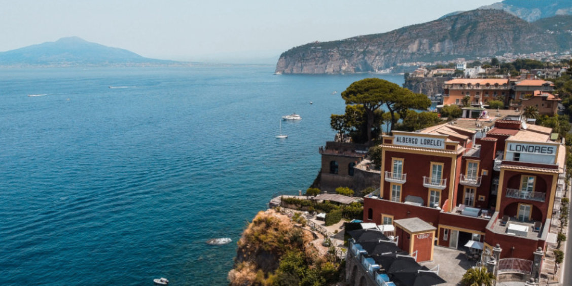 Vue panoramique de Sorrente avec hôtels sur les falaises, mer bleue et Vésuve au loin.