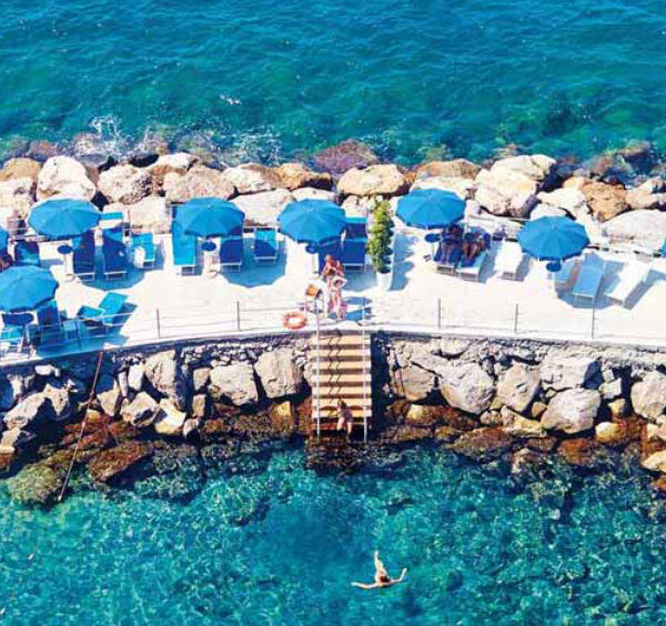 Plage aménagée à Sorrente avec parasols bleus, rochers et eau turquoise.