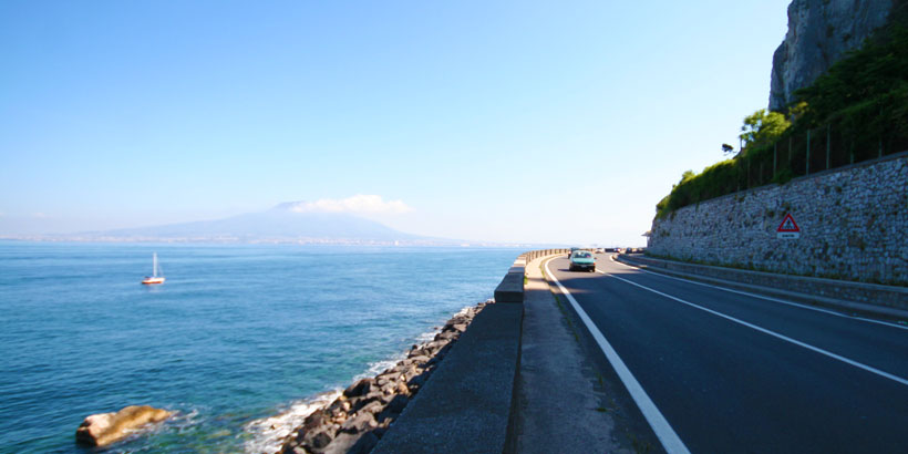 Route panoramique vers le Vésuve longeant la côte avec vue sur la mer et le volcan.
