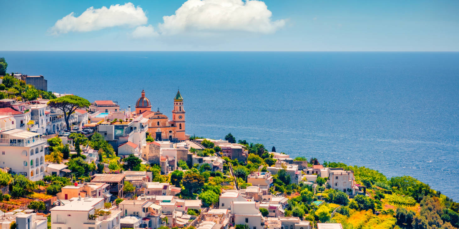 Village de Praiano avec église et panorama sur la côte amalfitaine sous un ciel ensoleillé.