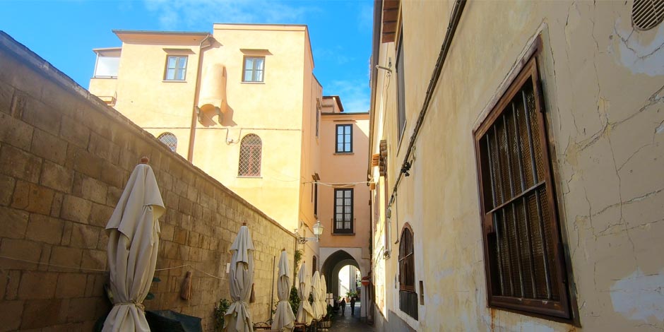 Via Pietà à Sorrente avec ruelle étroite, palais anciens et parasols fermés.