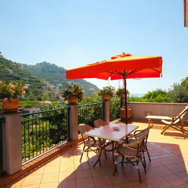 Terrasse ensoleillée de la Villa Anna avec table, parasol orange et vue sur les collines de Minori.