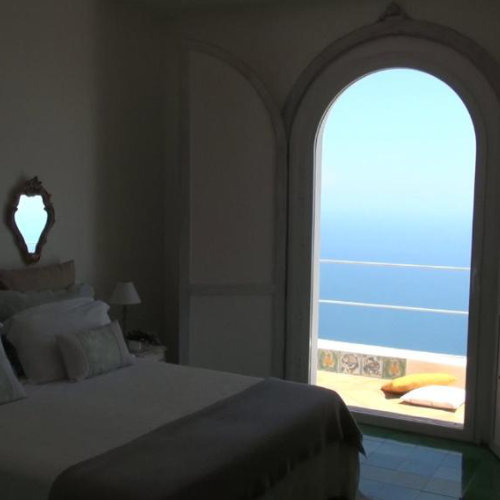 Chambre de la Villa Aramara à Furore avec grande porte ouverte sur la mer.