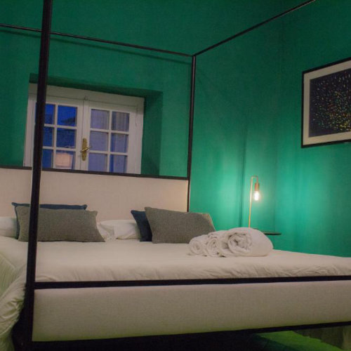 Chambre de caractère aux murs vert émeraude avec un lit à baldaquin moderne en métal noir et une lumière tamisée.