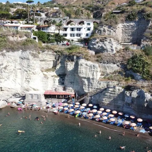 Vue aérienne de la plage de Cava Grado avec ses parasols bleus au pied des falaises.