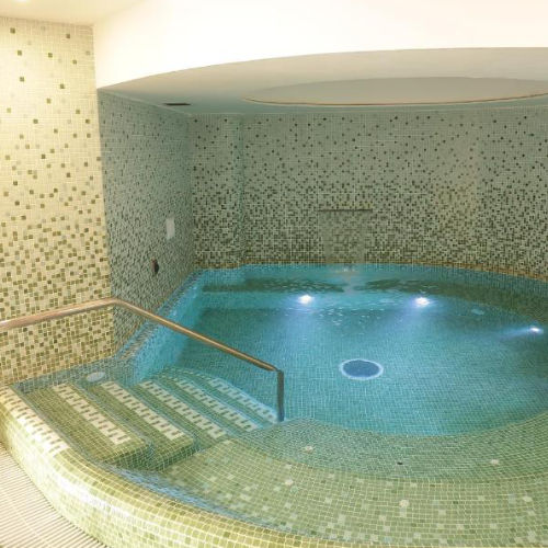 Piscine thermale intérieure décorée de mosaïques vertes.