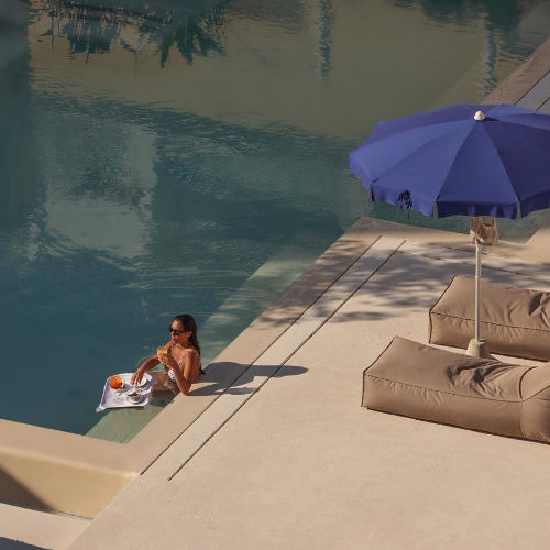 Une personne se relaxe dans la piscine de l'hôtel avec un cocktail sur un plateau.