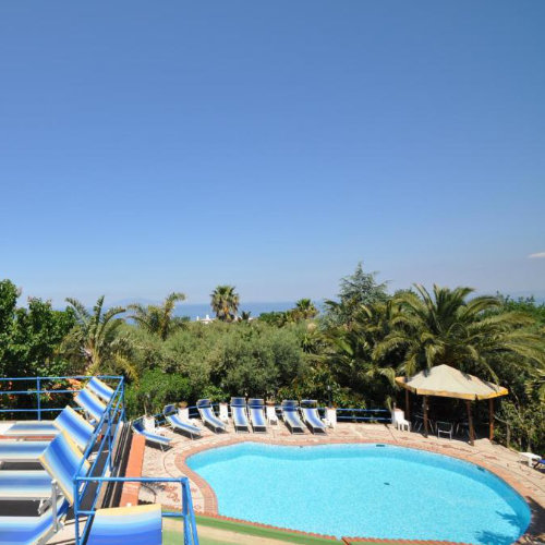 Piscine de la Villa Eva à Capri entourée de palmiers et d'un jardin luxuriant sous le soleil.