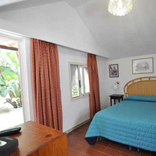 Chambre de la Villa Eva à Capri avec lit bleu, tête de lit en osier et rideaux colorés.