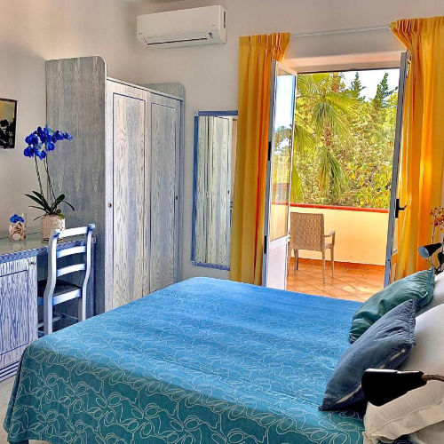 Chambre aux tons bleus et jaunes avec balcon à la Villa Flavio.