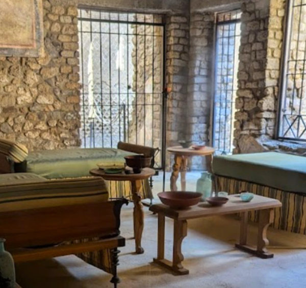 Salle de la Villa Impériale à Pompéi avec lits de banquet romains, petites tables et murs en pierre ancienne.