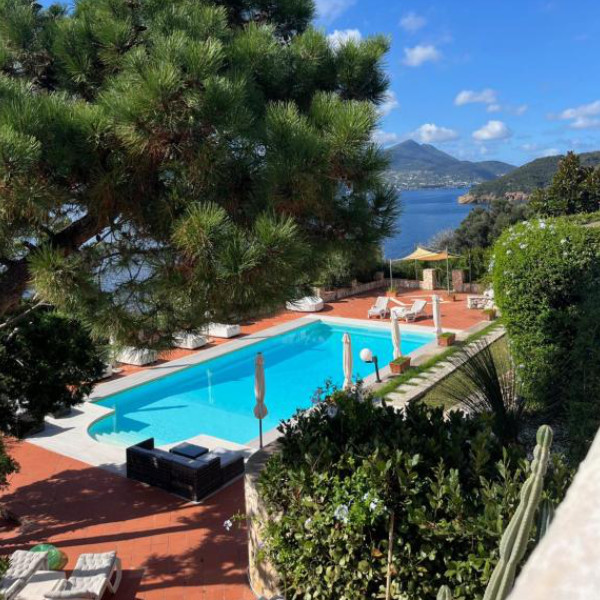 Grande piscine rectangulaire entourée d'un solarium en terre cuite avec vue panoramique sur la mer.