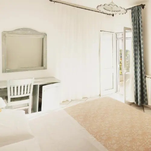 Chambre lumineuse et sobre avec un bureau blanc et accès au balcon.