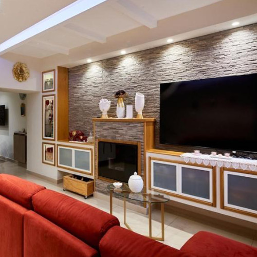 Espace salon de la Villa Nadia avec un canapé rouge et un mur de télévision en parement de pierre.