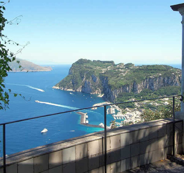 Vue panoramique sur le port et les falaises de Capri depuis la terrasse de la Villa San Michele, encadrée par des colonnes en pierre.