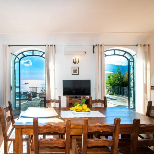 Salle à manger de Ville Olimpo à Positano avec grandes portes vitrées et vue sur la mer.