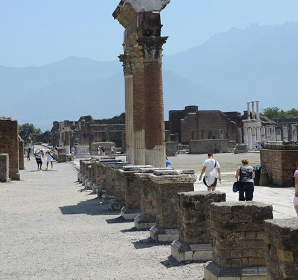 Visiteurs parcourant une rue bordée de colonnes antiques sur le site archéologique de Pompéi.