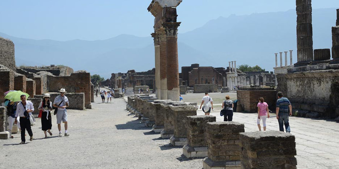 Visiteurs parcourant une rue bordée de colonnes antiques sur le site archéologique de Pompéi.