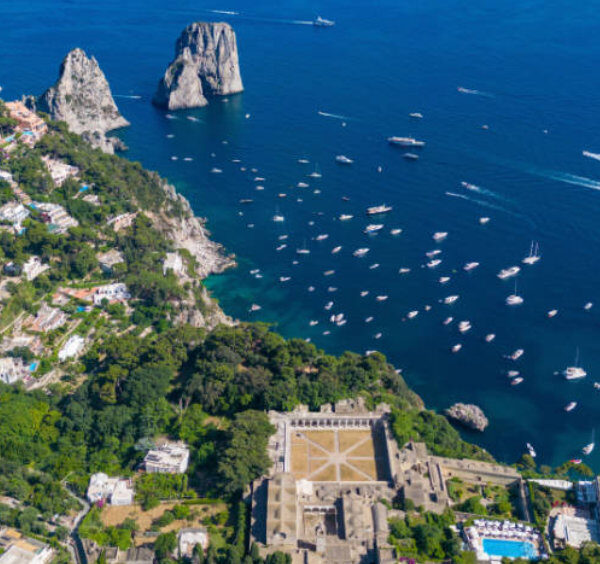 Vue aérienne spectaculaire des rochers Faraglioni à Capri avec de nombreux bateaux de plaisance sur une mer bleu azur.