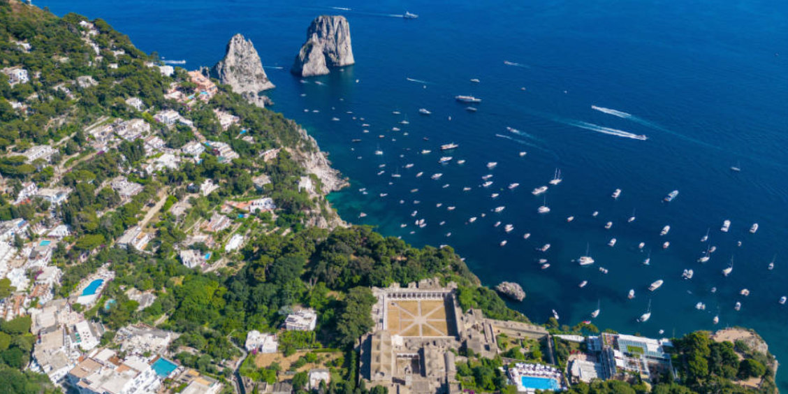 Vue aérienne spectaculaire des rochers Faraglioni à Capri avec de nombreux bateaux de plaisance sur une mer bleu azur.