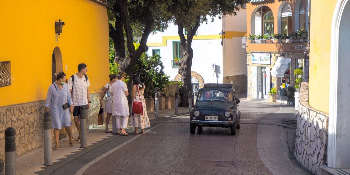 Rue étroite de la Côte Amalfitaine avec touristes, maisons colorées et voiture.