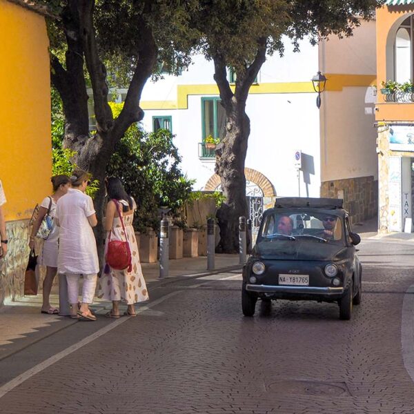 Rue étroite de la Côte Amalfitaine avec touristes, maisons colorées et voiture.