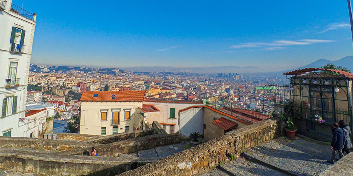 Vue panoramique de Naples depuis une colline avec centre historique, toits et Vésuve en arrière-plan.