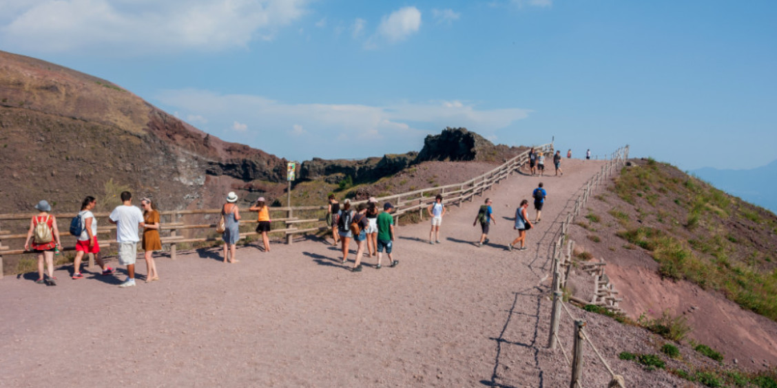 Visiteurs sur le sentier de randonnée du cratère du Vésuve en Campanie, entourés de paysages volcaniques secs.