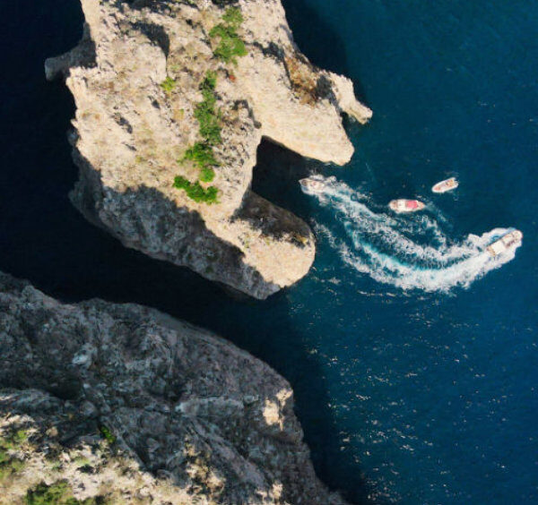 Vue aérienne verticale de bateaux passant à travers l'arche d'un des rochers Faraglioni à Capri.
