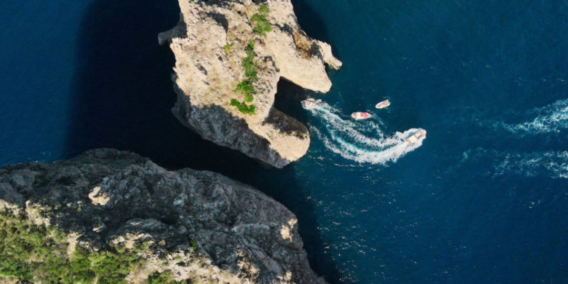 Vue aérienne verticale de bateaux passant à travers l'arche d'un des rochers Faraglioni à Capri.