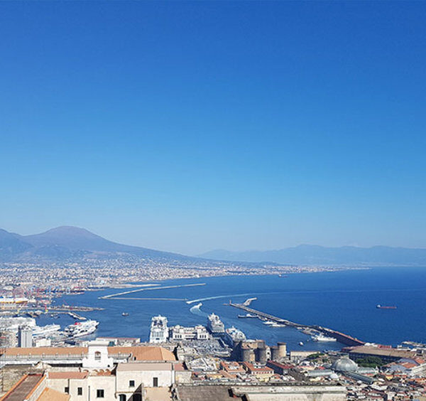 Vue panoramique de Naples avec port, centre-ville et Vésuve sous ciel bleu depuis les hauteurs.