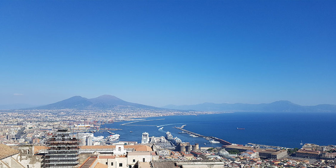 Vue panoramique de Naples avec port, centre-ville et Vésuve sous ciel bleu depuis les hauteurs.